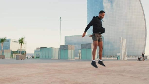 Young male athlete doing squats and jumping on the waterfront