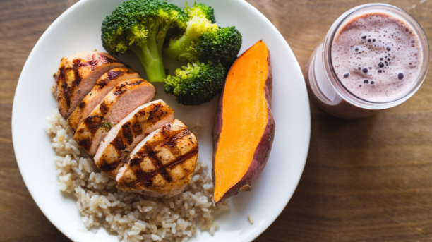 Balanced post-workout meal with grilled chicken breast, brown rice, steamed broccoli, sweet potato, and protein shake on wooden table